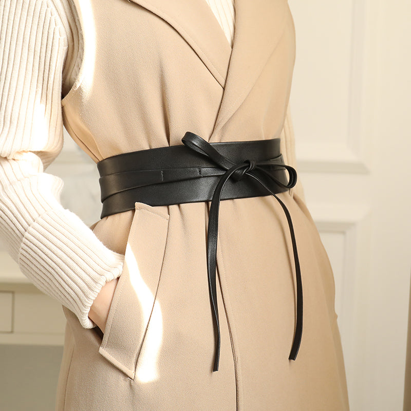Ceinture obi en cuir noir nouée sur une veste beige sans manches et un pull crème